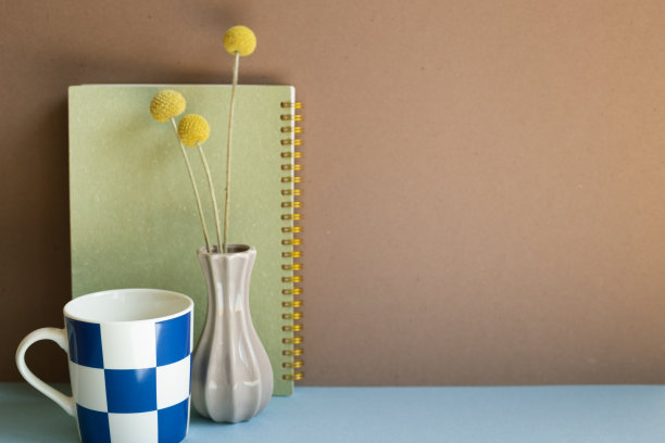 蓝色的桌子上放着笔记本、杯子和干花。棕色的背景墙图片下载