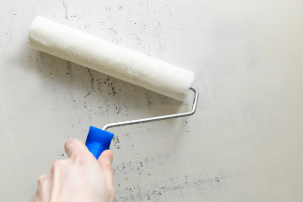 涂漆辊放在混凝土墙面上的男手中，复制空间。修理工具放在地板上图片下载