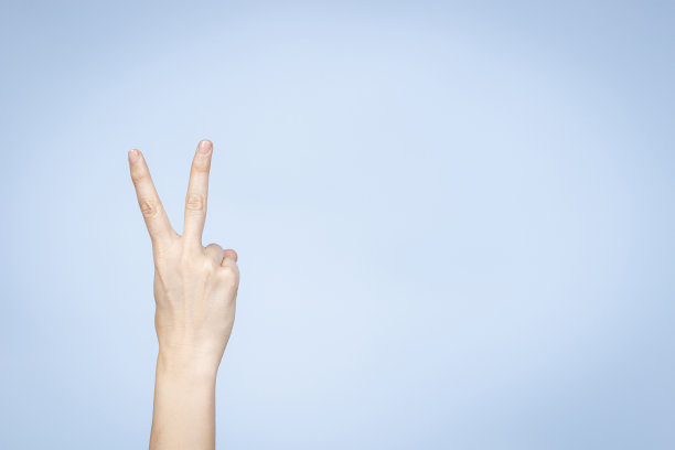 手的姿势。女人的手显示第二。手势表示胜利，和平。女人的手指着浅蓝色的背景与手指图片下载
