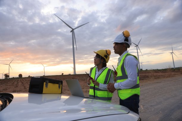 肖像男性和女性维护同事与安全PPE工作在风力涡轮机农场，可再生和绿色能源的概念图片下载