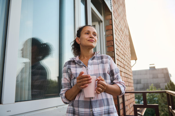 站在阳台上，眺望远方，享受阳光明媚的早晨咖啡的宁静女人图片下载