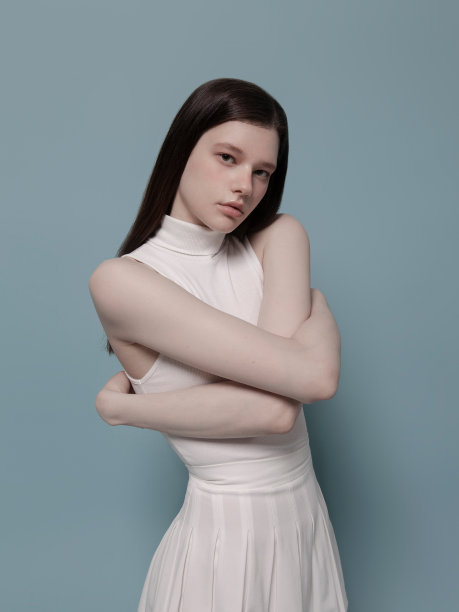 穿着可爱的白色无袖上衣和百褶裙的美丽的年轻女子，韩国风格的K-pop时尚，亚裔白人的混血美人，蓝色背景的时尚模特肖像图片下载