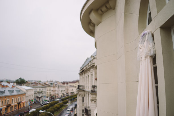 米色的婚纱挂在阳台上，背景是城市风光。多雨的婚礼。图片下载