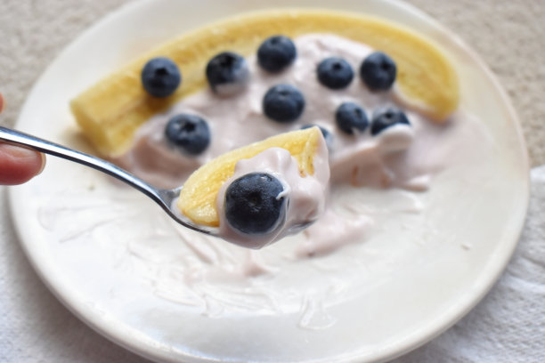 特写勺子新鲜可口的有机蓝莓，香蕉和酸奶的白色盘子。早上的健康饮食。图片下载