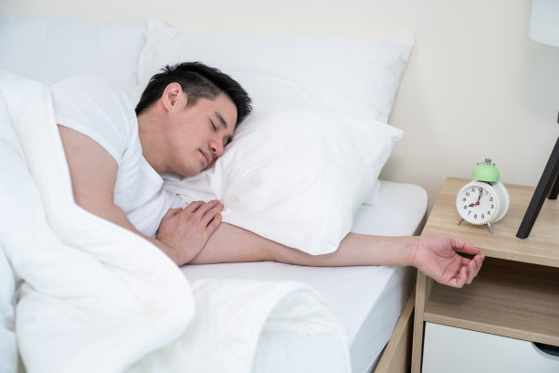 亚洲帅哥早上把闹钟关掉。帅男觉得又懒又累躺在卧室舒适的床上不顾噪音，一直睡不醒图片下载
