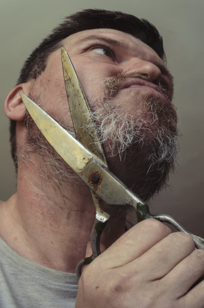 一个成年男子用一把巨大的旧剪刀剪自己的胡子。图片下载
