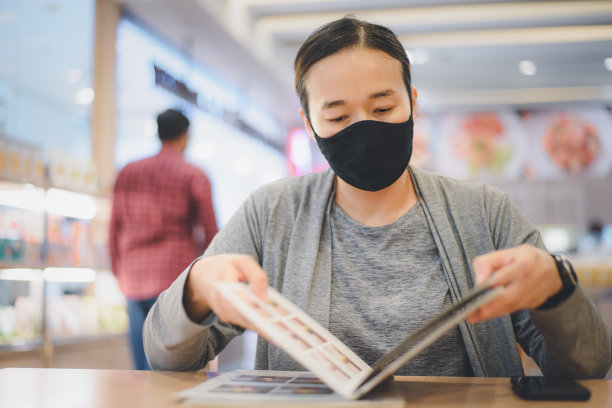 年轻的亚洲女性戴着外科口罩在餐厅。新冠肺炎带来的新常态和生活方式理念。图片下载