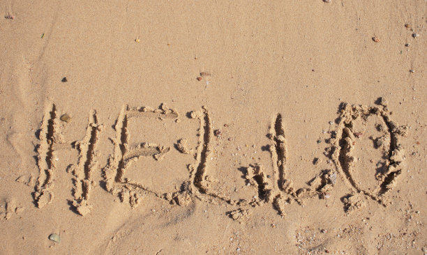 夏天，一个男孩在海边的沙滩上画着“你好”图片下载