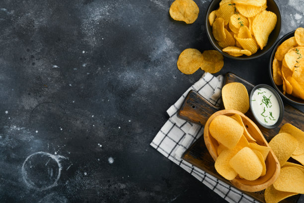 不健康的食物。零食。所有经典的土豆小吃，花生，爆米花，洋葱圈和咸椒盐脆饼，在黑色混凝土背景碗盘。对身材、心脏、皮肤、牙齿都不健康图片下载