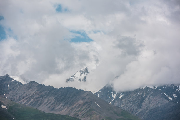 在阴雨多云的天空下，巨大的雪山山脉的戏剧性鸟瞰图。黑暗大气的高山风景与高雪山高峰在低云。阴沉的风景，山顶阴云密布。图片下载