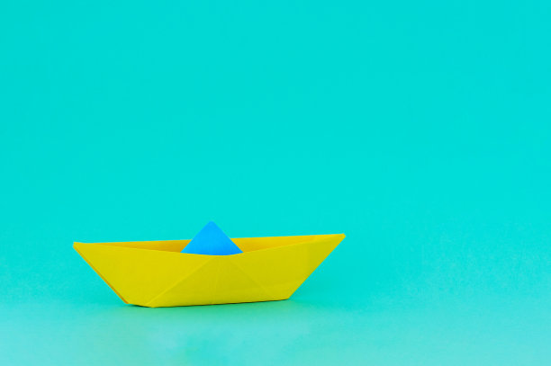 蓝绿色背景上的黄蓝色纸船。文本。图片下载