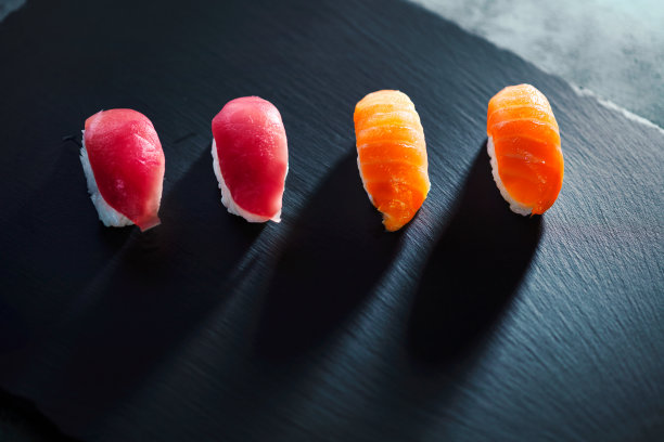 高角度的四个寿司部分躺在黑色纹理板。灯光和阴影效果。图片下载