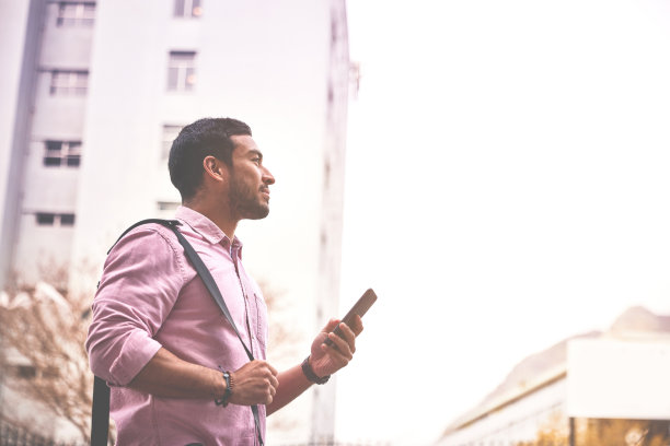 一个年轻的商人在城市背景下使用智能手机。商人一边走在城市的大街上，一边用手机上网图片下载