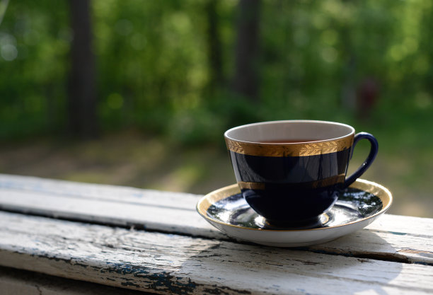 桌子上的一杯茶，背景是绿色的花园。新鲜的花草茶或绿茶，盛在漂亮的蓝色金边杯里。上午或下午健康天然芳香茶。静物与茶图片下载