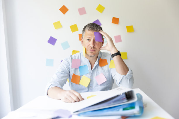 一个男人坐在办公室的墙壁前，有很多彩色的笔记，他自己也有很多笔记图片下载