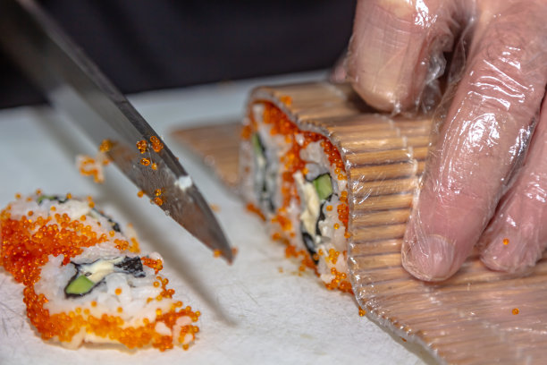 厨师的特写。男厨师用米饭、红鱼和牛油果做寿司和面包卷。图片下载