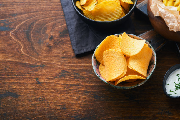 土豆corrugatedchips。快餐。脆薯片陶瓷黑色碗与酸奶油酱和洋葱在木制的立场上旧木制黑色背景。美国传统。热烧烤。俯视图图片下载