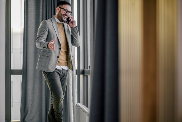 兴高采烈的企业家站在办公室的窗口用智能手机聊天图片下载