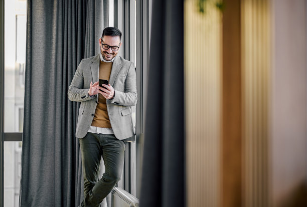 自信微笑的商人站在办公室用智能手机进行社交图片下载