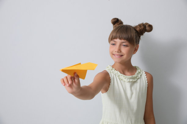可爱的小女孩在浅灰色的背景下玩纸飞机图片下载