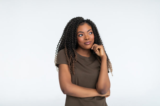 非裔美国女性穿着黄色毛衣，贴着白墙手托着下巴，侧视带着怀疑和怀疑的表情，怀疑和怀疑。图片下载