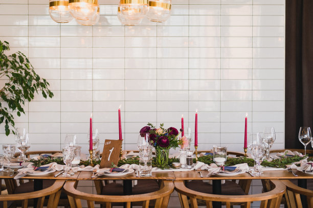 婚宴上的餐桌摆设。花卉组成与美丽的毛茛花和绿色植物，蜡烛，铺设和盘子在一个装饰的桌子。图片下载