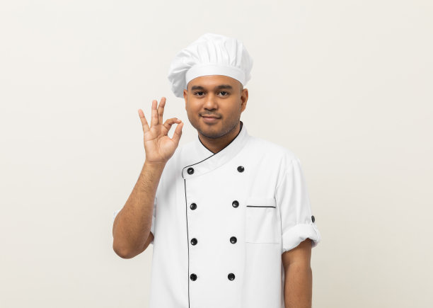 快乐年轻英俊的亚洲人厨师穿着制服戴着帽子站着张贴好的味道，高兴，美味的手势。印度人职业厨师或面包师，厨房、餐厅和酒店的人。图片下载