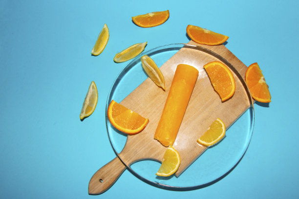 橙子冰淇淋放在一个透明的玻璃板上，橙子片和柠檬片放在一个盘子上，盘子旁边是一个木制的乡村板，这是一个创意的夏季概念图片下载