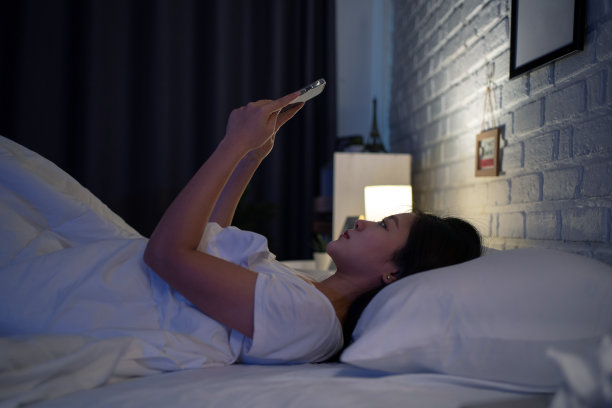 一名亚洲女性在晚上使用电话社交网络，她在床上。图片下载