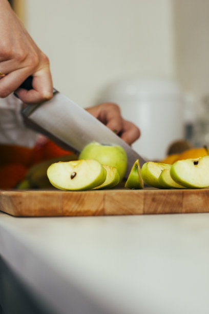 一个女人在白色的厨房里用菜刀把苹果切成片。以健康的早餐开始新的一天。健康有机食品。股票的照片。图片下载