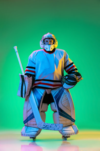 年轻男孩的肖像，曲棍球运动员在特殊的保护制服的守门员摆出孤立的绿色背景在霓虹灯。图片下载