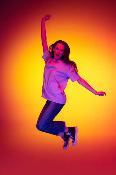 年轻开朗的女孩全身肖像，学生长头发跳跃孤立在橙色背景霓虹灯，过滤器。情感、青春、美丽的概念图片下载