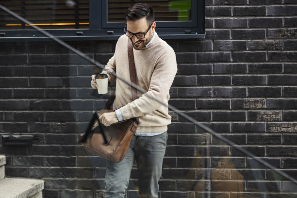 一个忙碌的男人在楼梯上寻找他的包里的东西，同时喝着咖啡。图片下载