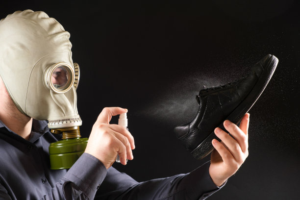 一个戴着防毒面具的男人用香水喷他的鞋子，解决脚和鞋子的难闻气味问题图片下载