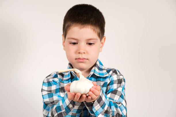 一个4岁的学龄前男孩在白色背景上拿着大蒜。图片下载