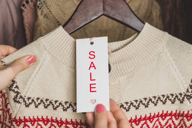 女顾客在服装店里看标签和文字销售选择带有圣诞装饰的毛衣。冬季购物打折、促销图片下载