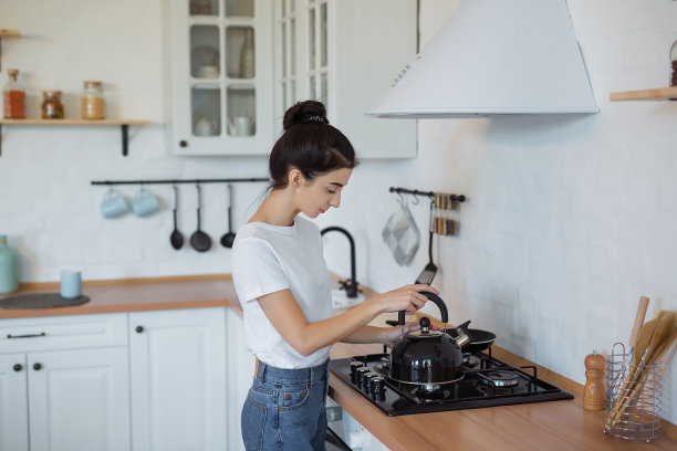 在现代阁楼厨房里，女人触摸炉子上的茶壶。拿着水壶的美女图片下载