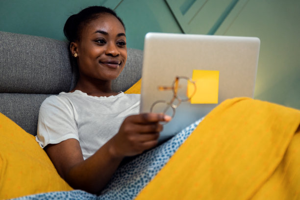 年轻的非洲裔美国女性躺在卧室的床上使用笔记本电脑。图片下载