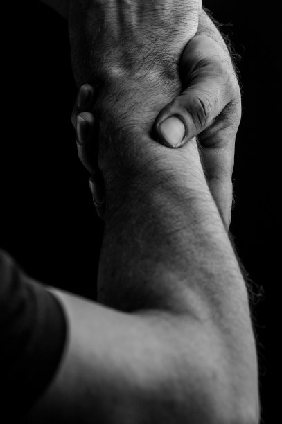 黑白特写：双手紧握彼此手腕，在黑色背景上象征帮助和支持图片下载