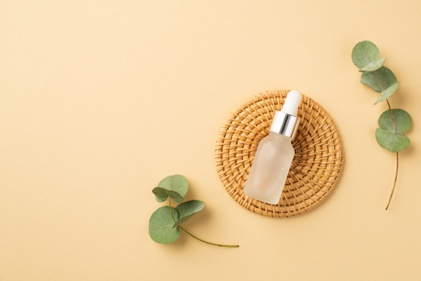 天然化妆品的概念。透明滴管瓶在柳条站和桉树叶子上孤立粉彩米色背景的俯视图照片图片下载