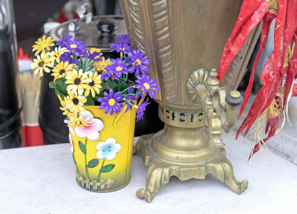 古色古香的铜制茶炊和带有黄色和紫色夏季花朵的cachepot。图片下载