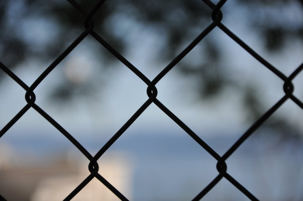 铁丝网栅栏的抽象图案镜头，背景是模糊的彩色城市。摘要背景模糊的金属丝栅栏。铁丝网:用金属丝制成的用于保护的栅栏或笼子图片下载
