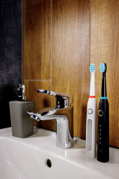 浴室的水槽上放着两把电动牙刷，还有一个灰色的肥皂分配器。镀铬水龙头和水槽。浴室内部和配件概念图片下载