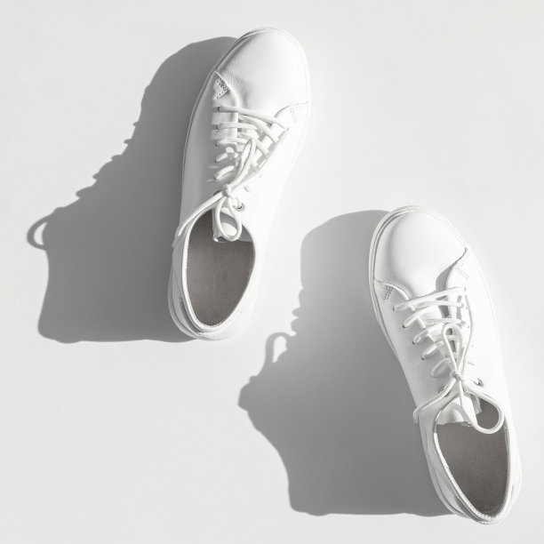 白色女性的皮革运动鞋与太阳阴影在白色背景顶视图。时尚青年运动鞋，运动鞋，真皮鞋履。简约的鞋店广告时尚风格图片下载