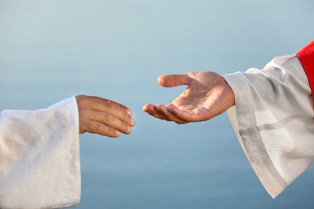 一个人在户外靠近水的地方伸手去抓耶稣的手，特写图片下载