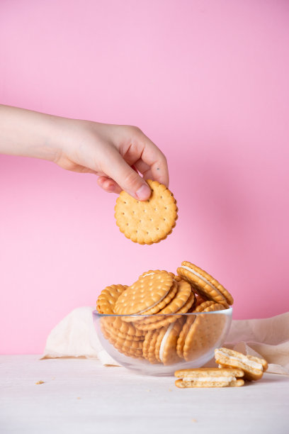 孩子的手从粉红色背景的玻璃碗里拿起一块饼干。早餐和快餐的概念。图片下载