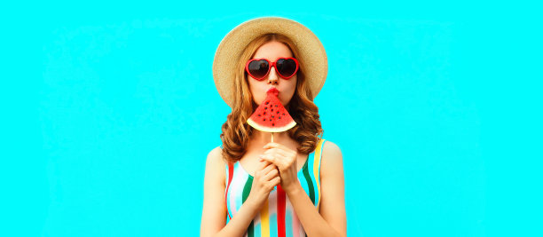 夏天的肖像年轻女子吮吸冰淇淋形状的西瓜片戴着草帽，红色的心形状的太阳镜在蓝色的背景，空白的拷贝空间的广告文字图片下载
