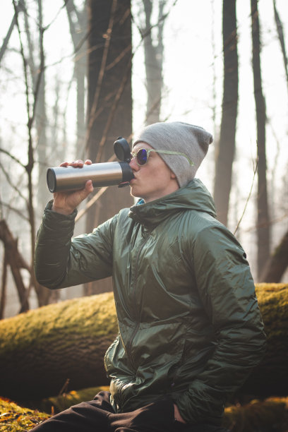 有经验的徒步旅行者坐在荒野的树干上，在散步间隙喝着热水瓶里的热茶。真实的人们发现欧洲森林的生物多样性。真正的微笑图片下载