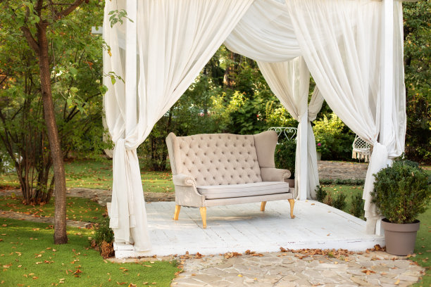装饰户外露台。户外休闲凉亭。在花园里有一个讲台，上面放着普罗旺斯风格或乡村风格的沙发。婚礼装饰。带有白色窗帘的夏日凉亭。浪漫的凹室图片下载