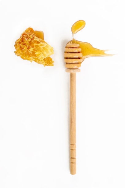 白色背景上有一块蜂巢的蜂蜜木勺。有机新鲜液态蜂蜜。健康的食物图片下载